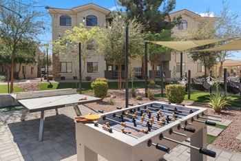 A foosball table is in the middle of a patio with a picnic table and a building in the background.